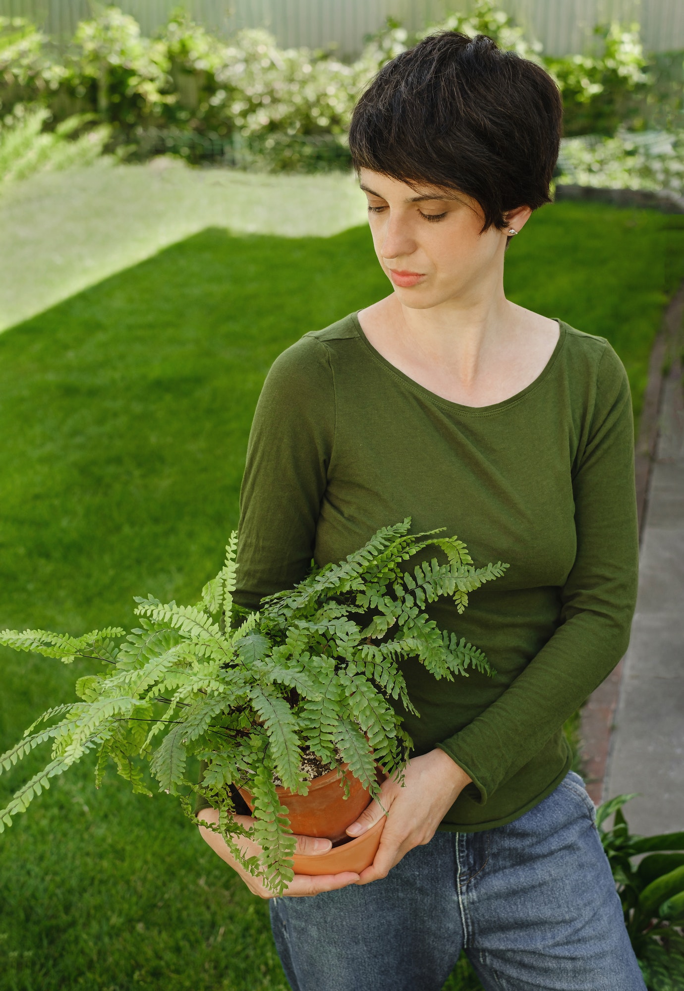 Woman holding houseplant fern over green lawn