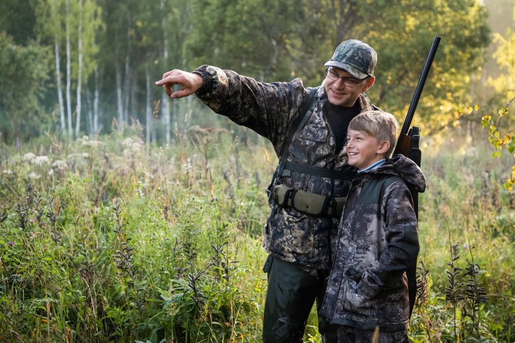 A young boy on the hunt with an experienced instructor in the forest.