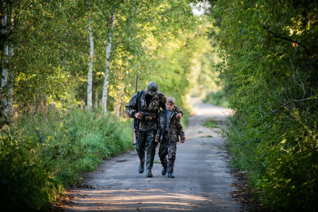 Hunters with hunting equipment going away through rural forest at sunrise during hunting season in