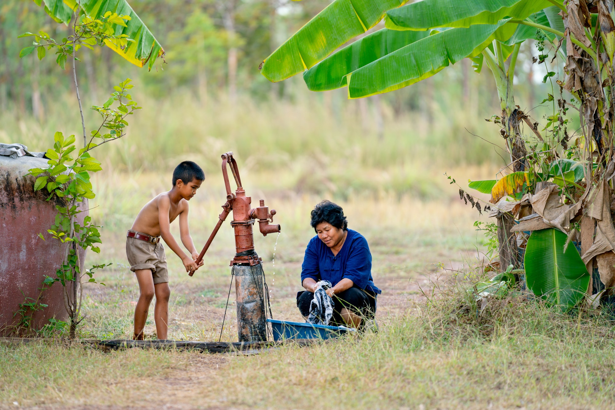 Asian boy help her mother or senior woman to wash black cloths using underground water