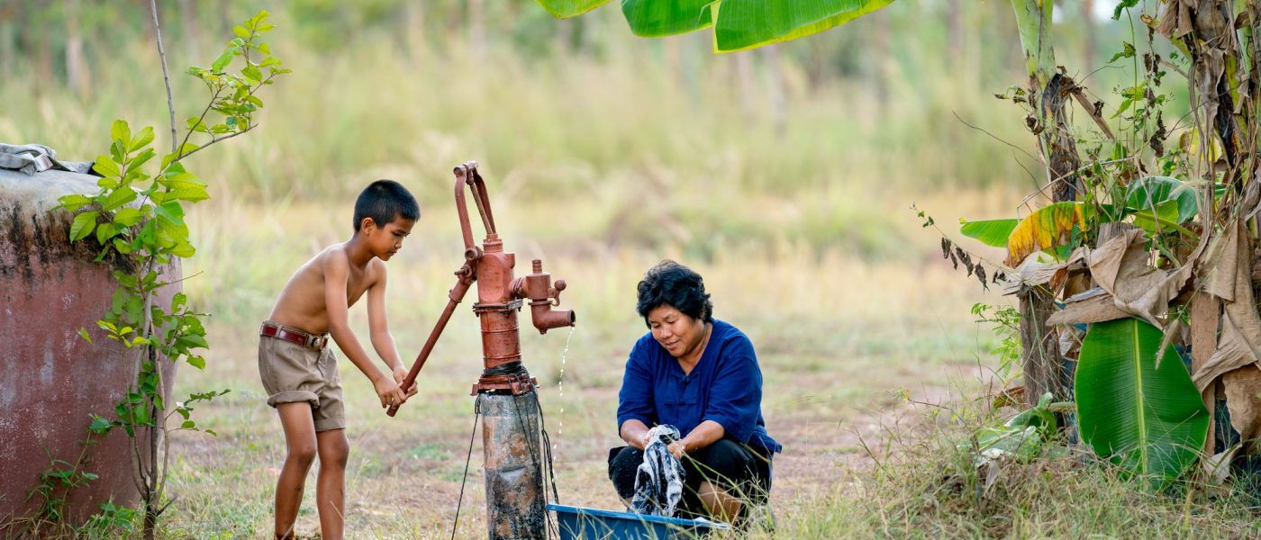 Asian boy help her mother or senior woman to wash black cloths using underground water