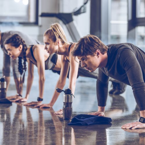 group of athletic young people in sportswear doing push ups or plank at the gym, group fitness